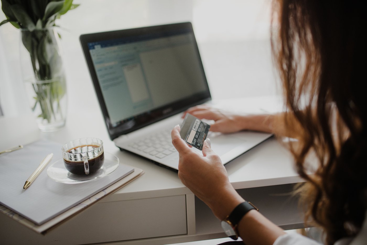 A woman holding a credit card while working at a laptop