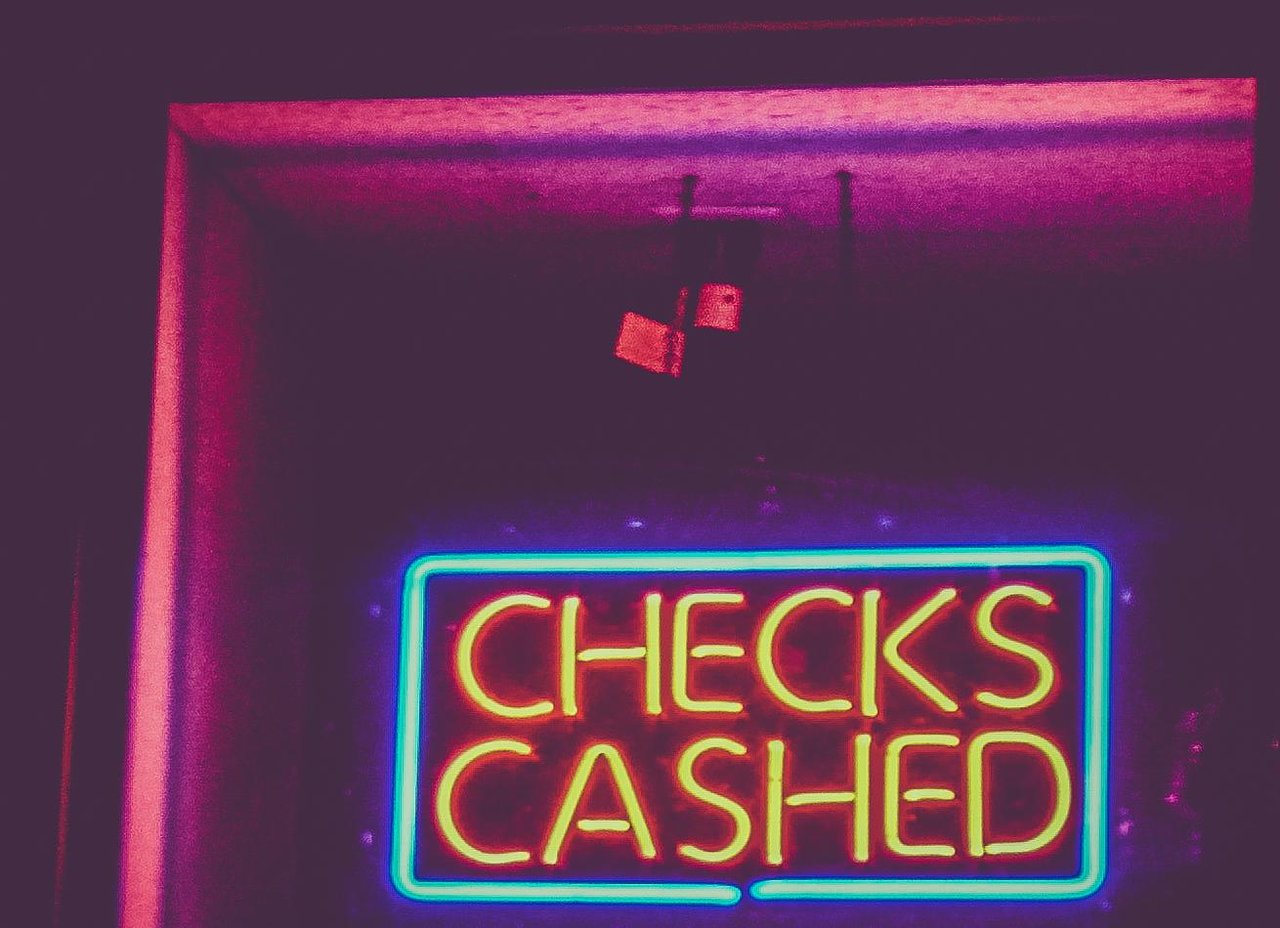 A neon Checks Cashed sign glowing above a storefront doorway at night