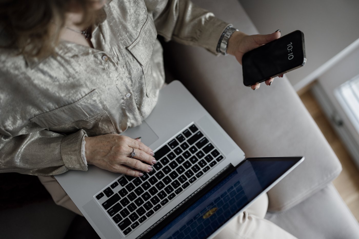 A person holding a smartphone while sitting with a laptop