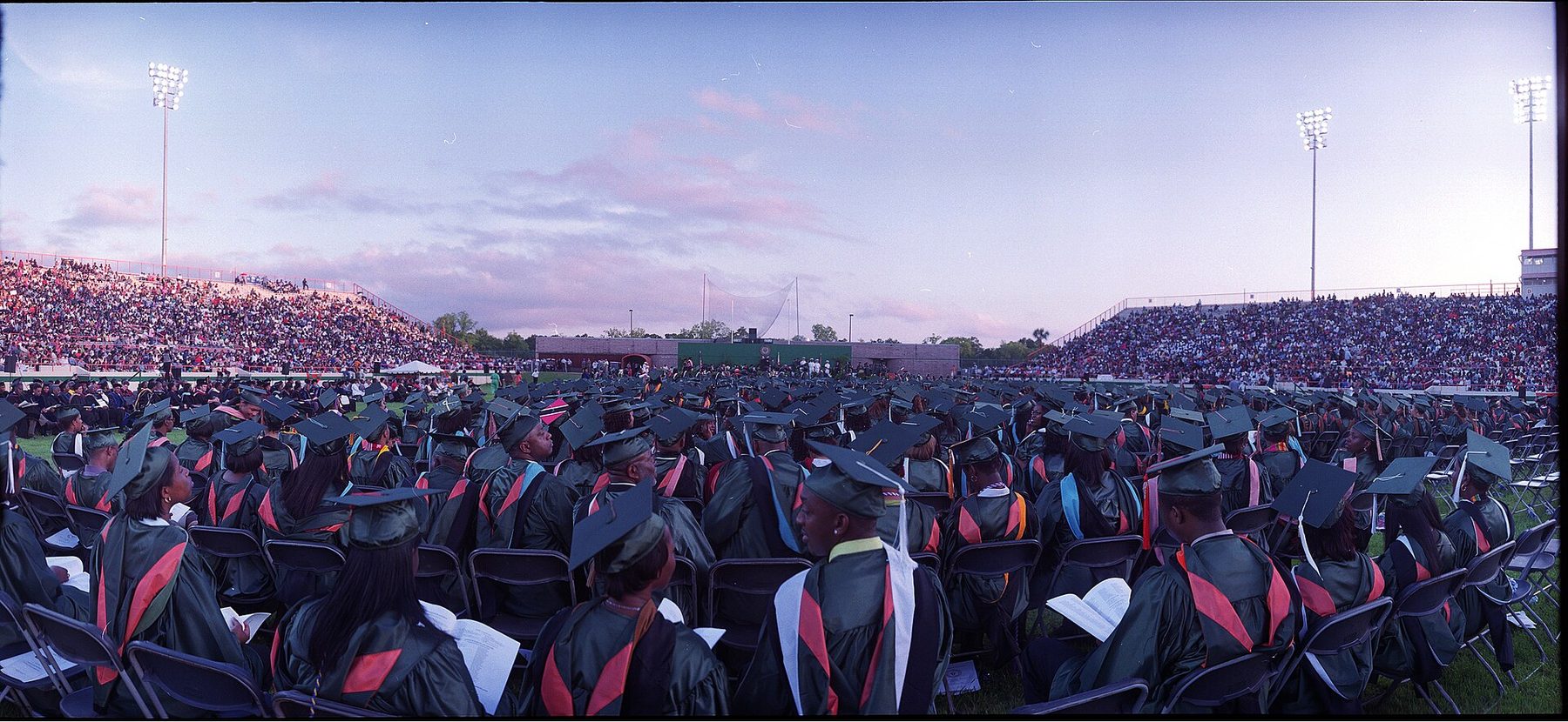A packed stadium of college graduates in caps and gowns