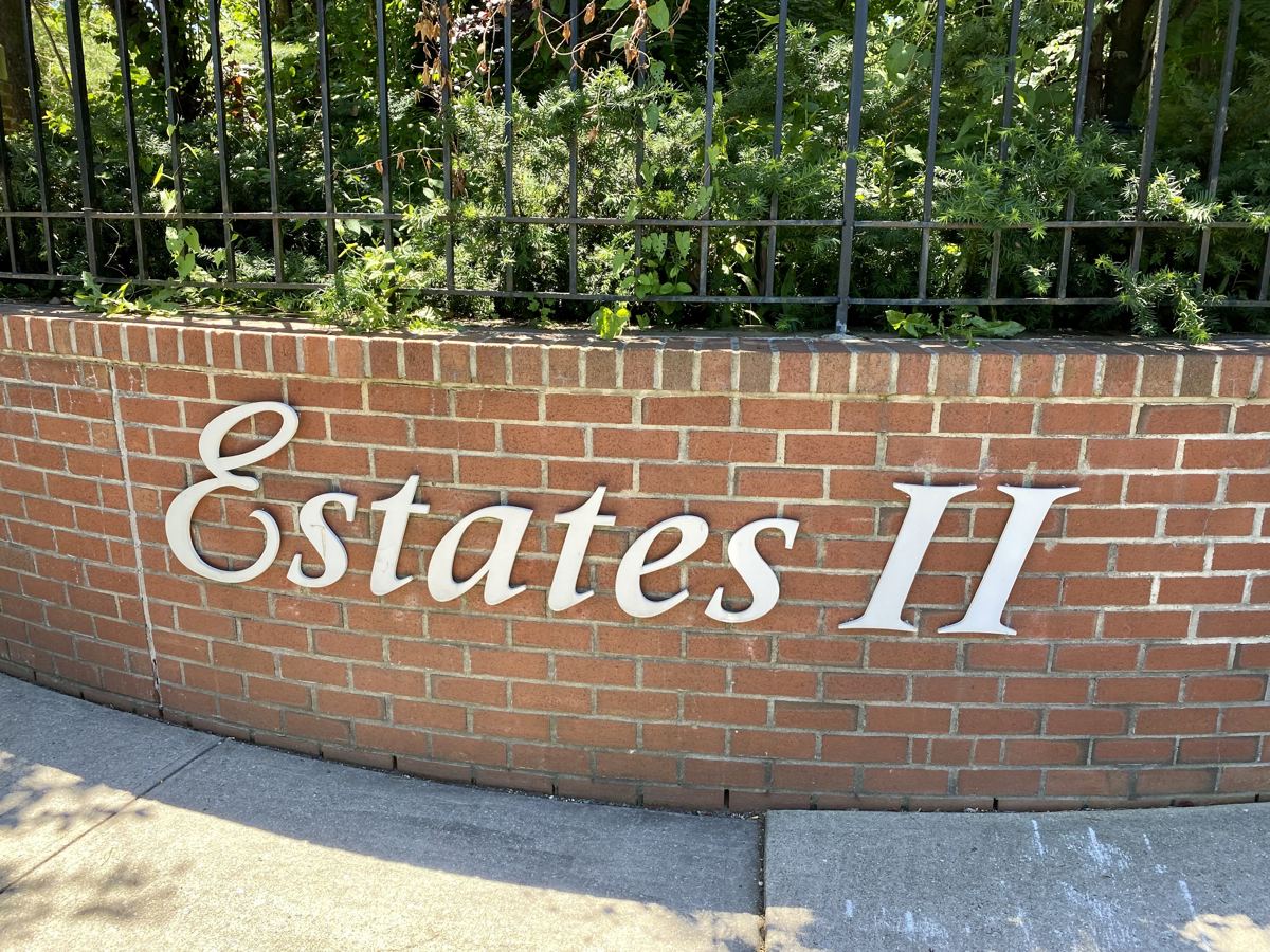 A brick entrance wall with a planned community's name and a wrought iron fence