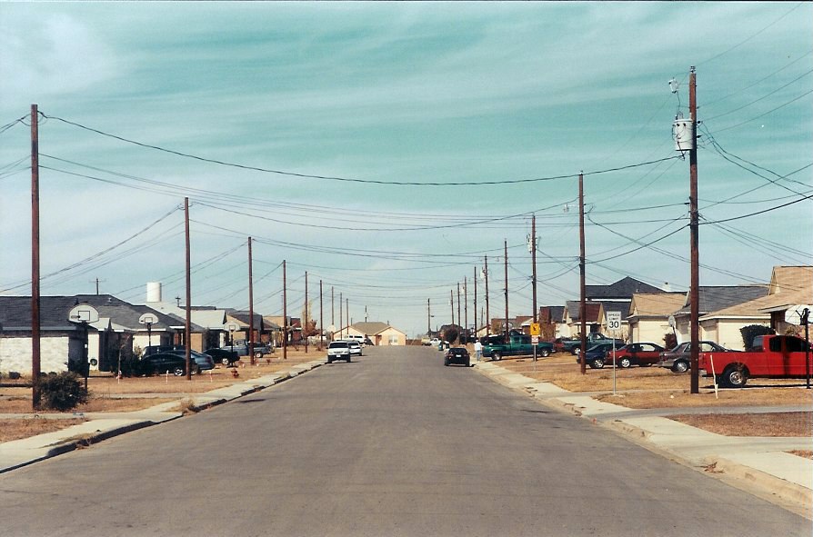 A typical suburban residential street in the United States, lined with single-family houses and cars