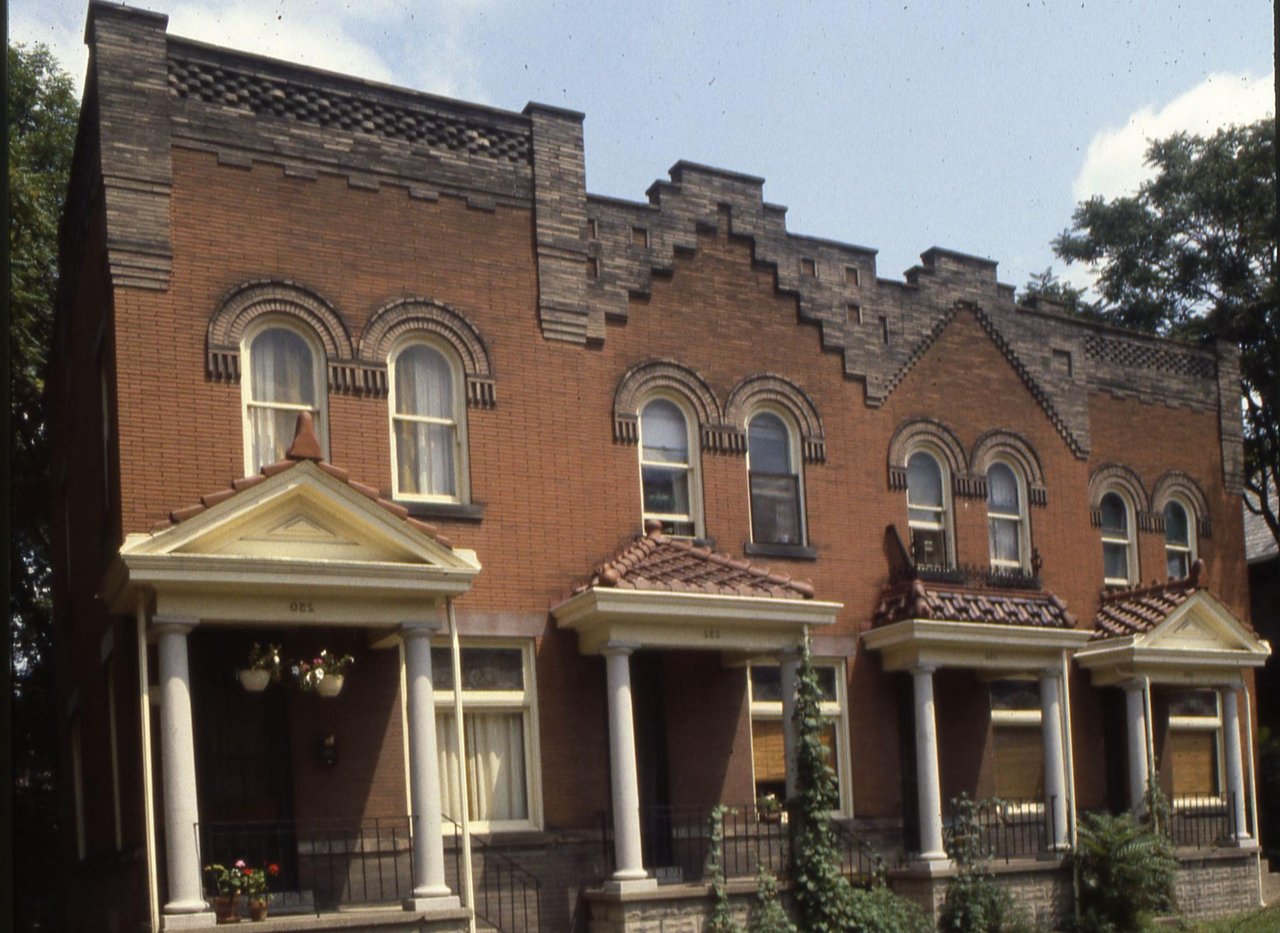 A row of brick apartment buildings with covered front porches along a residential street